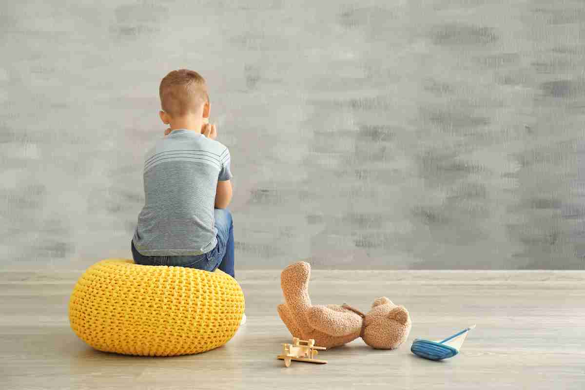 Niño sentado mirando a la pared en un cuarto vacio.